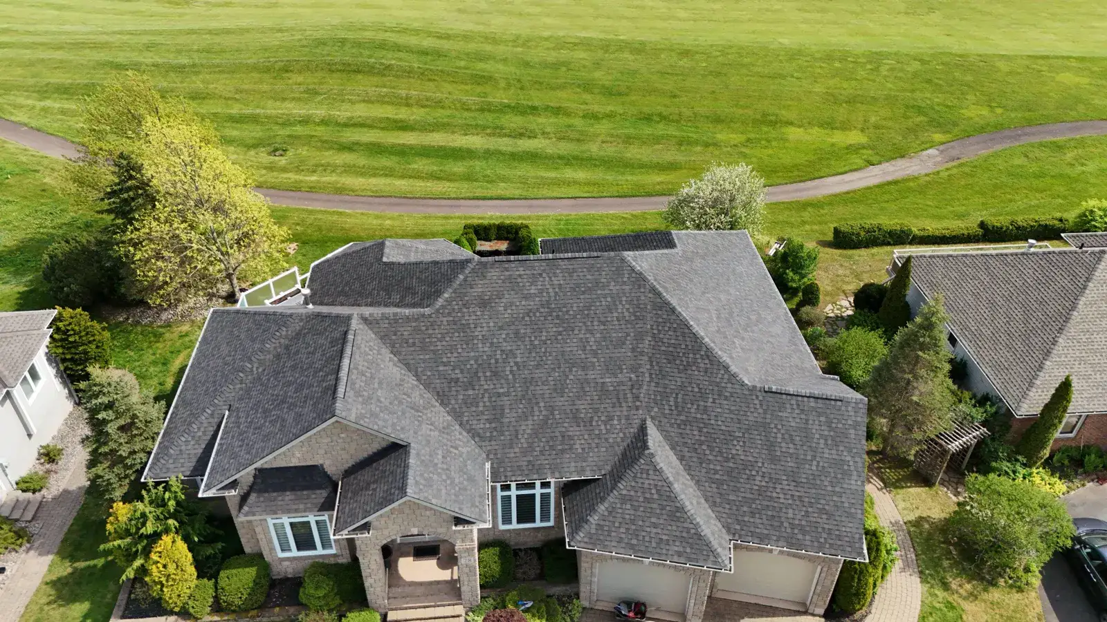Finished architectural shingle roof on a stone estate beside a golf fairway, from the air