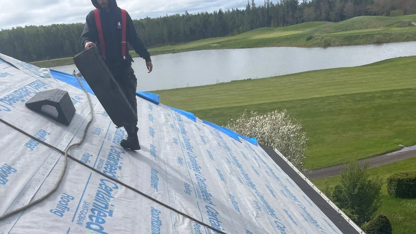 Harnessed roofer crossing fresh CertainTeed underlayment during a roof replacement in Moncton