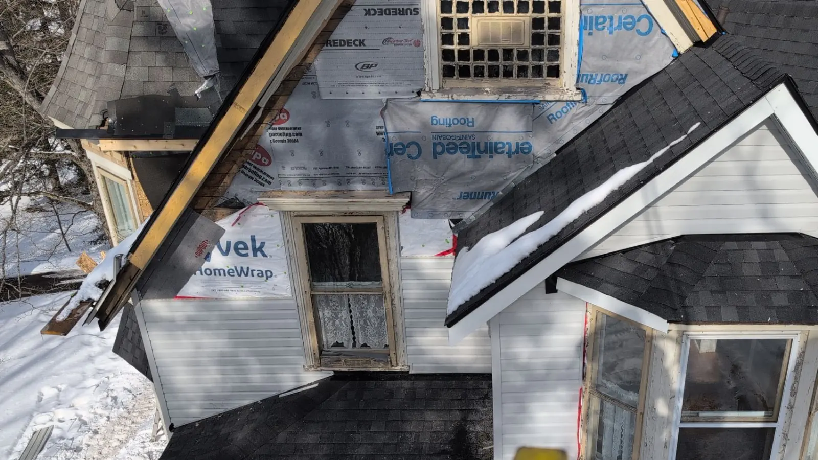 Winter reroof underway in New Brunswick: new shingle planes down, CertainTeed underlayment and house wrap on the dormers, snow on the ground